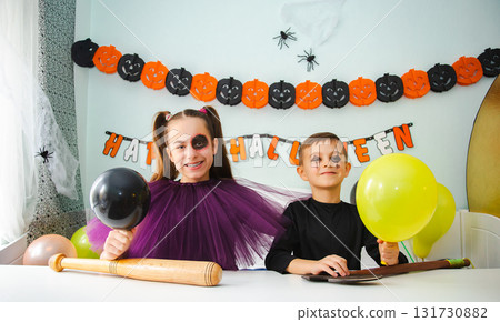 Two kids getting ready for Halloween. One girl applies makeup while boy inflates balloon. 131730882