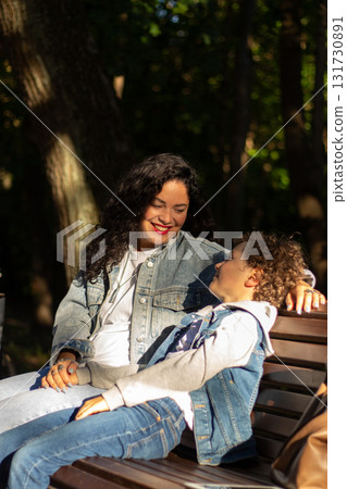 Portrait of young Caucasian single mother hugging her cute small son outside in park spending time on summer day together. Motherhood concept. Portrait of young Caucasian single mother hugging her cute small son outside in park spending time on summer day together. Motherhood concept. 131730891