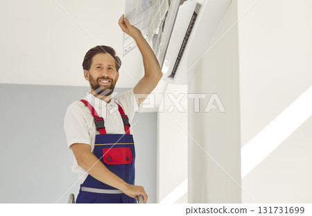 Portrait of electrician looking at camera and smiling maintaining air conditioner. 131731699