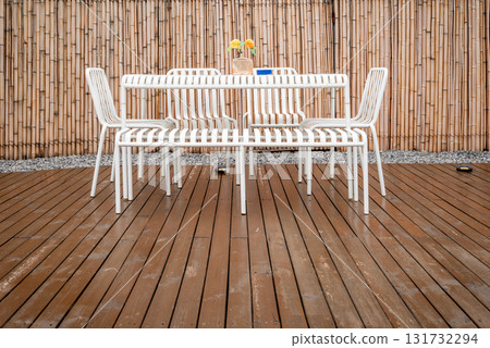 Outdoor dining area with white chairs and bamboo backdrop 131732294