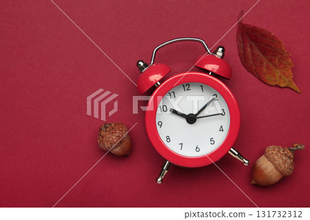 Red alarm clock, acorns and autumn leaves on red background. Daylight saving time end Red alarm clock, acorns and autumn leaves on red background. Daylight saving time end 131732312
