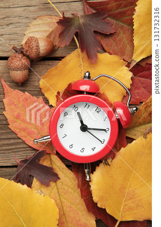 Red alarm clock, acorns and autumn leaves on grey wooden background. Daylight saving time end 131732316