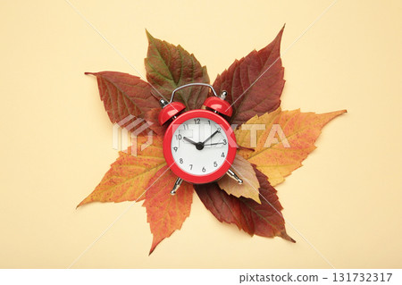 Red alarm clock, acorns and autumn leaves on beige background. Daylight saving time end Red alarm clock, acorns and autumn leaves on beige background. Daylight saving time end 131732317