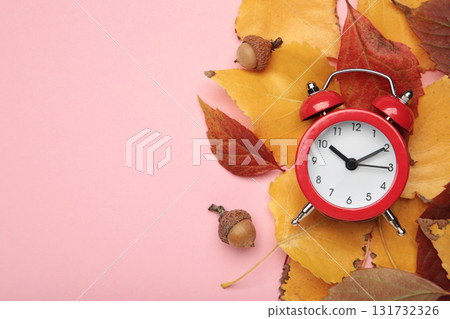 Red alarm clock, acorns and autumn leaves on pink background. Daylight saving time end Red alarm clock, acorns and autumn leaves on pink background. Daylight saving time end 131732326