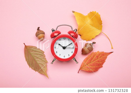 Red alarm clock, acorns and autumn leaves on pink background. Daylight saving time end Red alarm clock, acorns and autumn leaves on pink background. Daylight saving time end 131732328