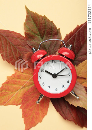Red alarm clock, acorns and autumn leaves on beige background. Vertical photo Red alarm clock, acorns and autumn leaves on beige background. Vertical photo 131732334