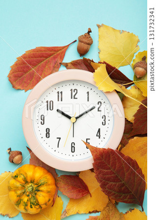 Red alarm clock, acorns and autumn leaves on blue background. Daylight saving time end 131732341