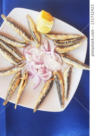 small deep-fried fish with lemon and herbs on a white plate 131732423