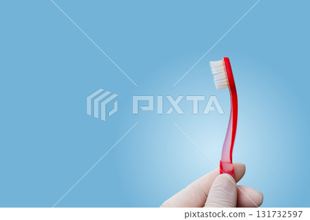 Bright red toothbrush held against soft blue background. 131732597