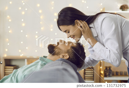 Beautiful young brunette woman wants to kiss her beloved man sitting on the sofa at home in the living room. Beautiful young brunette woman wants to kiss her beloved man sitting on the sofa at home in the living room. 131732975