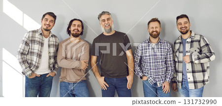 Group of happy men models wearing casual clothes standing by gray wall background Group of happy men models wearing casual clothes standing by gray wall background 131732990