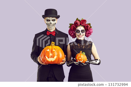 Happy couple dressed in skeleton costumes holding Halloween pumpkins and smiling 131732994