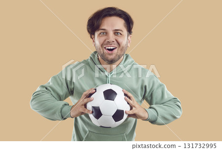 Soccer fan happy excited young man holding football ball in hands on beige background. Soccer fan happy excited young man holding football ball in hands on beige background. 131732995