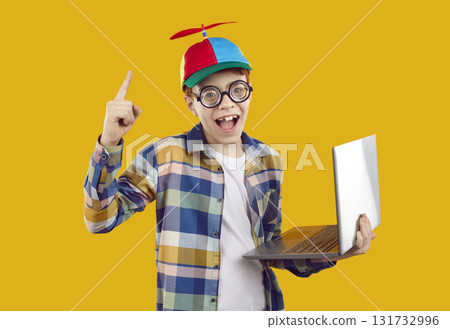 Funny happy school child in propeller cap has genius idea while using laptop computer Funny happy school child in propeller cap has genius idea while using laptop computer 131732996