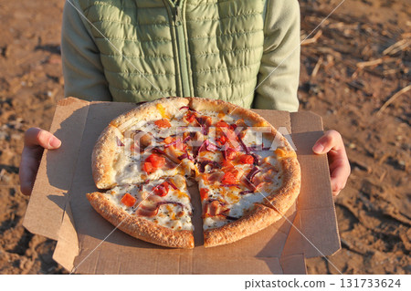 Unrecognizable child holding pizza paper box on beach in sunset light Unrecognizable child holding pizza paper box on beach in sunset light 131733624