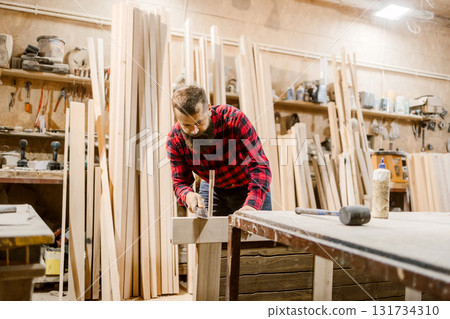 Carpenter working diligently in a woodworking shop on a rustic project surrounded by timber Carpenter working diligently in a woodworking shop on a rustic project surrounded by timber 131734310