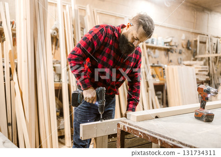 Craftsman using a power drill to work on wooden boards in a workshop during the day Craftsman using a power drill to work on wooden boards in a workshop during the day 131734311