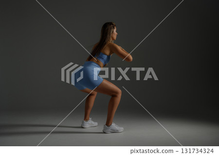 Woman performing squats in a fitness studio with dramatic lighting to enhance her posture and strength during workout 131734324