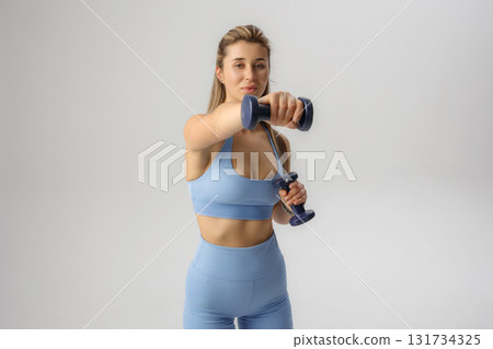 Fitness enthusiast performs dumbbell exercises indoors in stylish workout attire during daylight hours 131734325