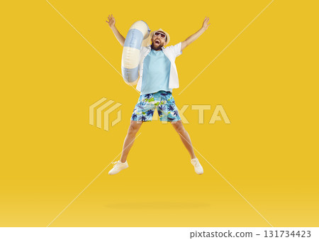 Cheerful male vacationer with inflatable beach circle jumping high on orange studio background. 131734423