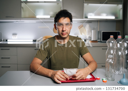 Portrait of gardening enthusiast wearing safety glasses examining fertilizer packet while preparing nutrient solution for vertical hydroponic system, highlighting innovative urban farming techniques. 131734700