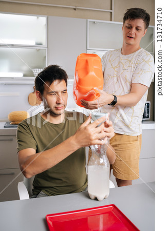 Vertical portrait of two gardeners preparing fertilizer for plants in home kitchen, mixing water and nutrients in plastic bottle using funnel and watering can. Concept of sustainable cultivation. Vertical portrait of two gardeners preparing fertilizer for plants in home kitchen, mixing water and nutrients in plastic bottle using funnel and watering can. Concept of sustainable cultivation. 131734710