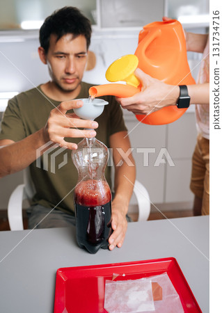 Biology students mixing fertilizer solution, using watering can, funnel and plastic bottles in laboratory setting, demonstrating precise scientific methodology. Concept of sustainable cultivation. 131734716