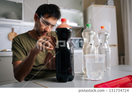 Focused chemist wearing protective eyewear mixing plant fertilizer solutions, handling precise syringes and chemical containers in professional laboratory setting. Concept of urban farming. 131734724
