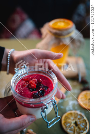 closeup of hand with berry panna cotta dessert and red cherry sauce in glass jar 131735524