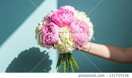 A hand holds a beautiful, elegant bouquet of fresh flowers against a bright, light blue background. A hand holds a beautiful, elegant bouquet of fresh flowers against a bright, light blue background. 131735536