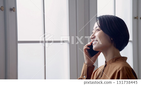 Woman making a phone call by the window Woman making a phone call by the window 131738445