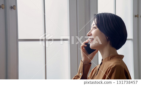 Woman making a phone call by the window Woman making a phone call by the window 131738457