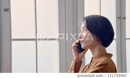 Woman making a phone call by the window Woman making a phone call by the window 131738461