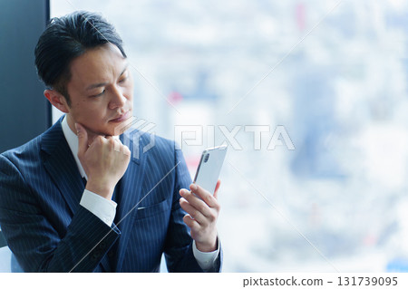 A 40-year-old office worker using a smartphone with a troubled expression 131739095