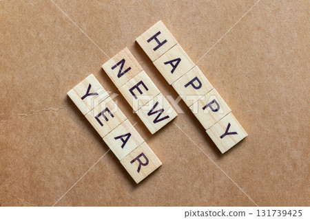 Wooden letter tiles arranged to spell HAPPY NEW YEAR on a brown textured background Wooden letter tiles arranged to spell HAPPY NEW YEAR on a brown textured background 131739425