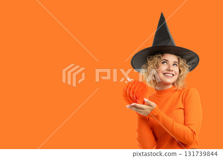 Woman in orange sweater and witch hat holds pumpkin decoration 131739844