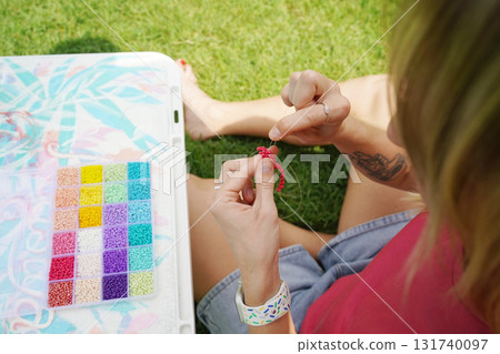 Young woman beading colorful bracelets outdoors in a park Young woman beading colorful bracelets outdoors in a park 131740097