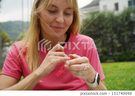 Young woman beading colorful bracelets outdoors in a park Young woman beading colorful bracelets outdoors in a park 131740098