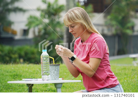 Young woman beading colorful bracelets outdoors in a park 131740101