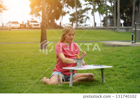 Young woman beading colorful bracelets outdoors in a park Young woman beading colorful bracelets outdoors in a park 131740102