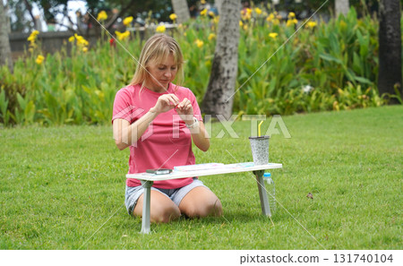 Young woman beading colorful bracelets outdoors in a park 131740104