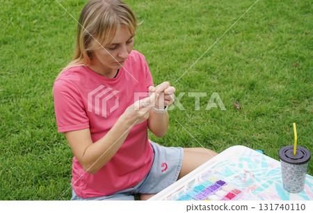 Young woman beading colorful bracelets outdoors in a park Young woman beading colorful bracelets outdoors in a park 131740110