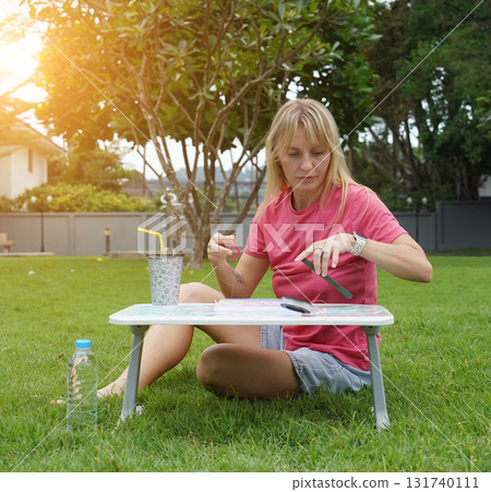 Young woman beading colorful bracelets outdoors in a park Young woman beading colorful bracelets outdoors in a park 131740111
