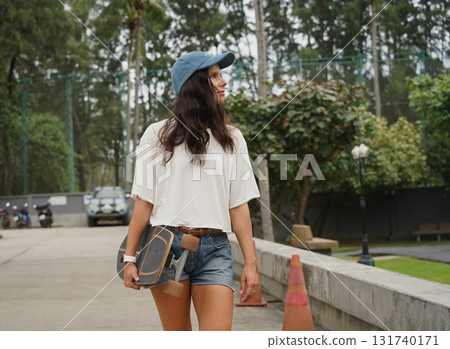 A woman is walking at the city park while carrying a skateboard in her hands 131740171