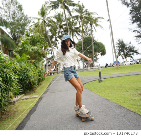 A young woman is skillfully riding a skateboard down a scenic park 131740178