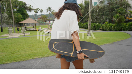 A woman is walking at the city park while carrying a skateboard in her hands 131740179