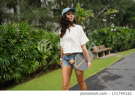 A woman is walking at the city park while carrying a skateboard in her hands A woman is walking at the city park while carrying a skateboard in her hands 131740182