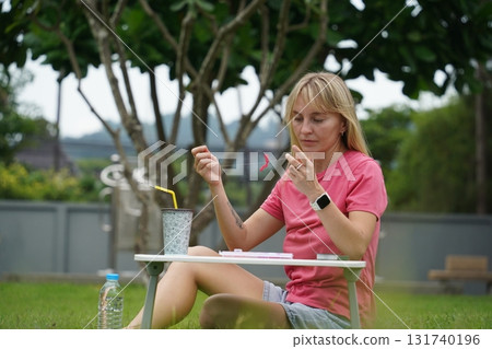 Young woman beading colorful bracelets outdoors in a park 131740196