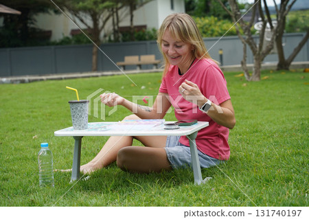 Young woman beading colorful bracelets outdoors in a park 131740197