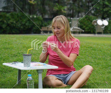 Young woman beading colorful bracelets outdoors in a park 131740199